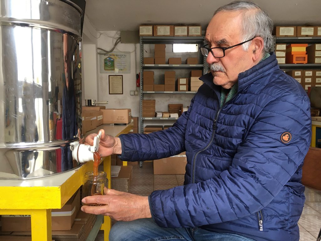 L'apicoltore Fernando versa il miele da un contenitore di metallo, in un barattolino di vetro.